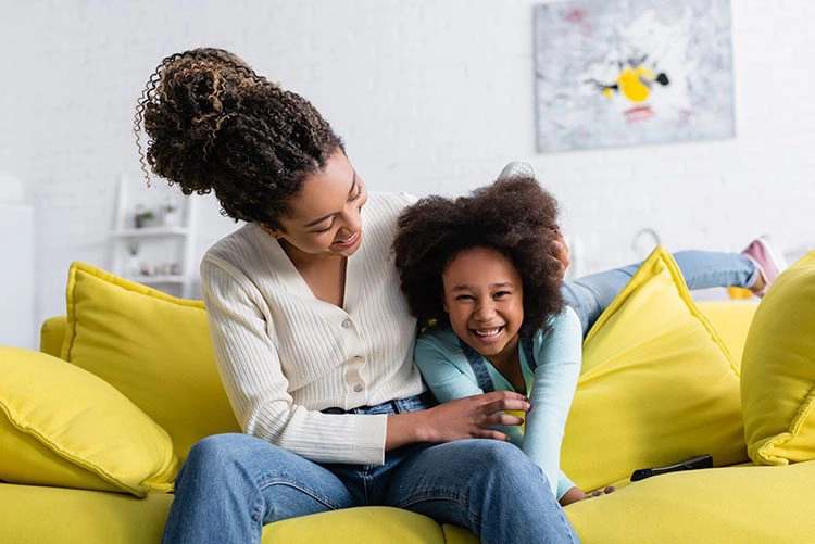 mother and daughter laughing on their couch in their home