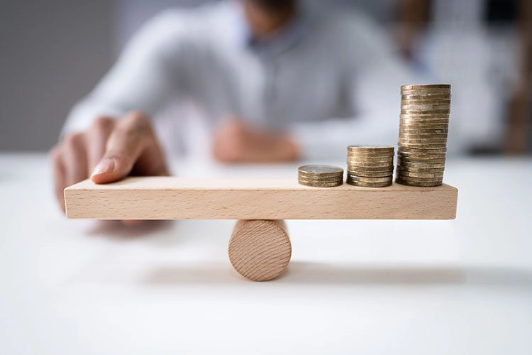 person using his finger to even the weight of money on a scale