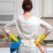 Why Ants Persist in a clean home: 5 Reasons. A woman stands in a kitchen ready to deep clean with cleaning supplies.